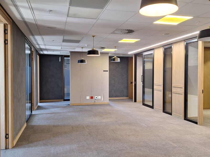 Modern open-plan office space featuring high-quality carpet tiles, suspended ceilings with integrated lighting, and sleek glass-partitioned private offices with timber accents.