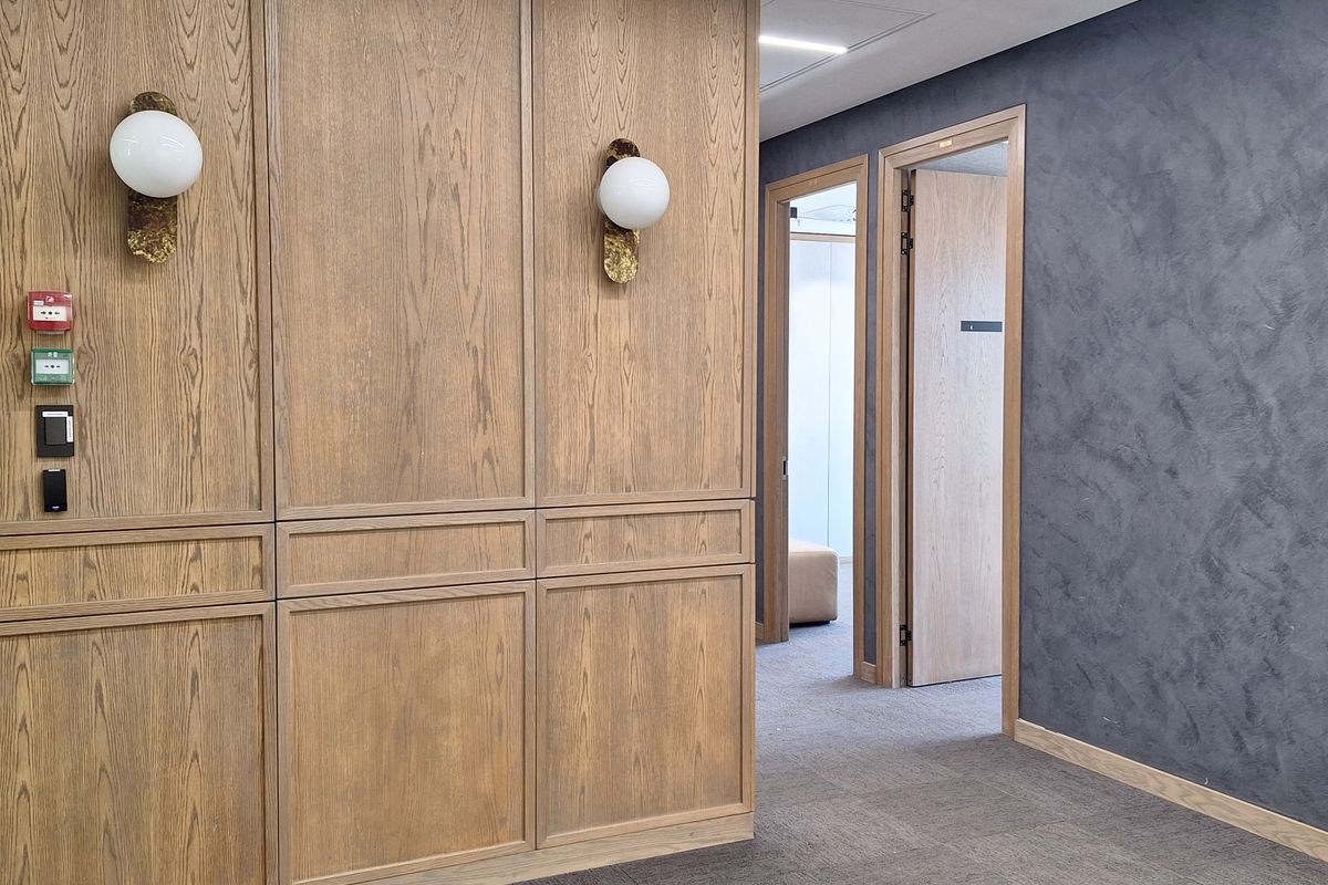 A modern office hallway featuring elegant wood paneling, textured feature walls, and integrated wall sconces with high-quality carpet flooring.