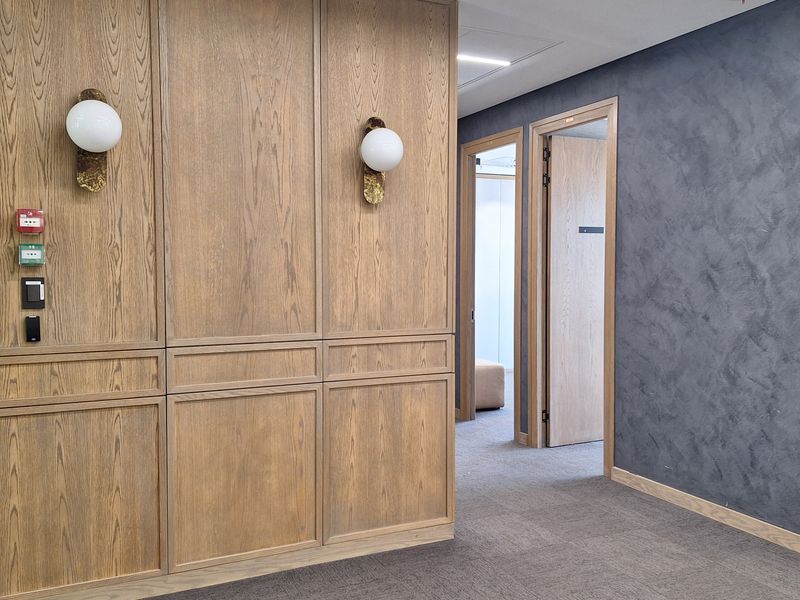 A modern office hallway featuring elegant wood paneling, textured feature walls, and integrated wall sconces with high-quality carpet flooring.
