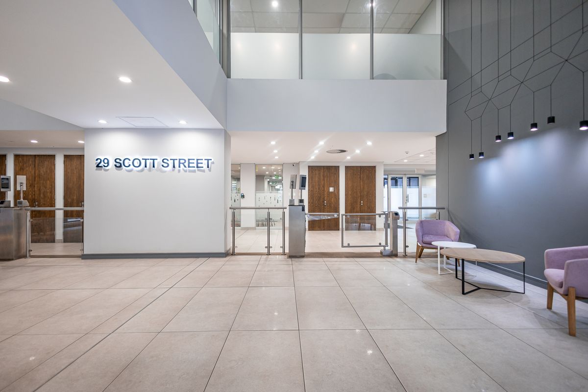 Modern office building entrance lobby featuring high ceilings, tiled flooring, security turnstiles, and professional glass partitioning.