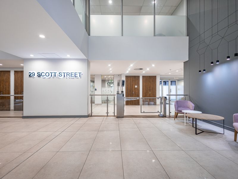 Modern office building entrance lobby featuring high ceilings, tiled flooring, security turnstiles, and professional glass partitioning.