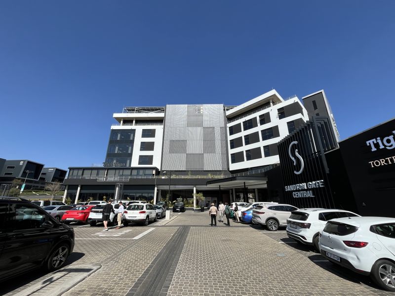 Modern commercial office building facade featuring contemporary architectural design, glass elements, and a paved parking area at the entrance.