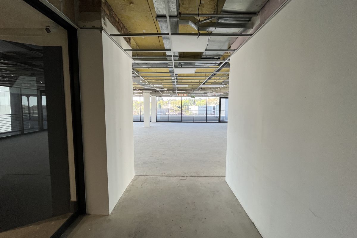 An open-plan office space currently in a shell condition with exposed ceiling infrastructure and large windows providing natural light.
