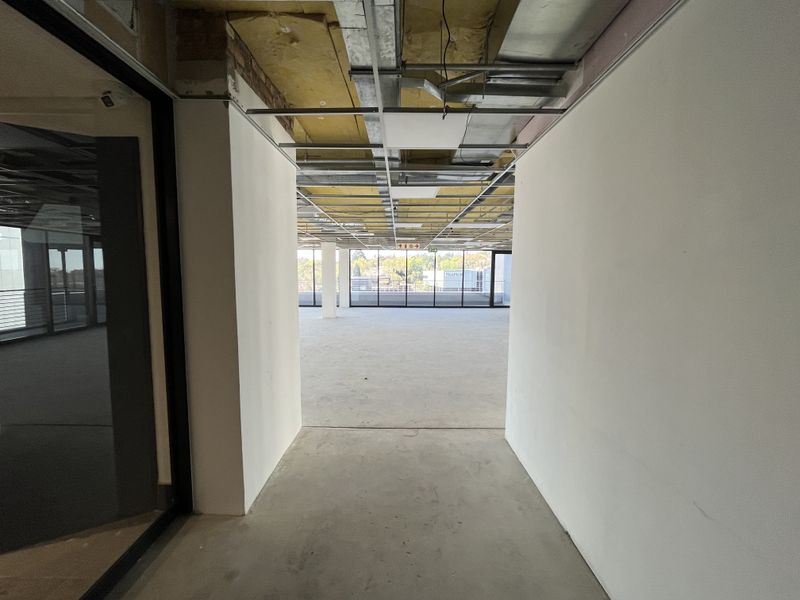 An open-plan office space currently in a shell condition with exposed ceiling infrastructure and large windows providing natural light.