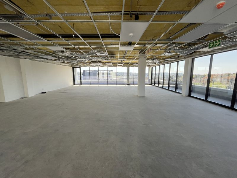 An expansive, open-plan office space currently in a shell condition with floor-to-ceiling windows and an unfinished ceiling grid.