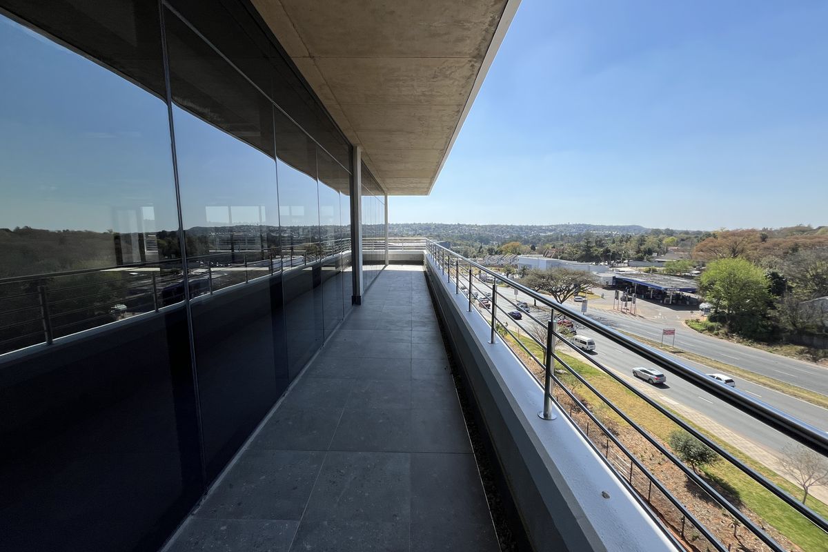 A modern, spacious office balcony featuring sleek glass curtain walls, stainless steel railings, and high-quality tiled flooring with expansive views.