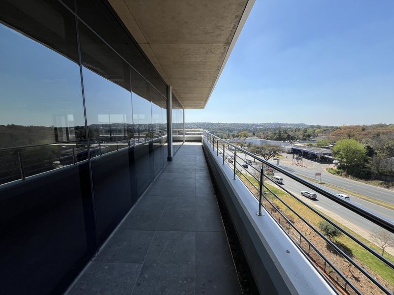 A modern, spacious office balcony featuring sleek glass curtain walls, stainless steel railings, and high-quality tiled flooring with expansive views.