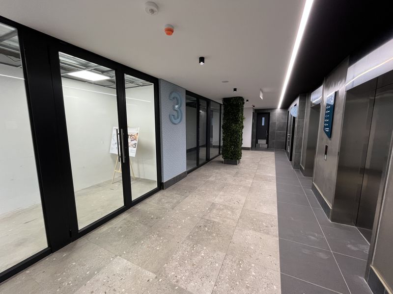Modern office building hallway featuring stone tile flooring, glass-partitioned office entrances, and a professional elevator lobby area.