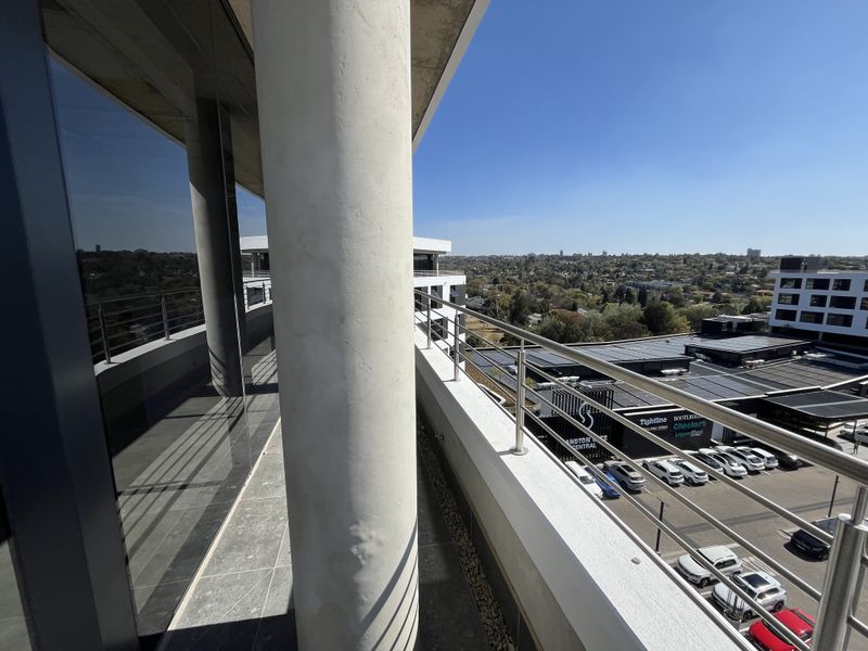 A modern balcony featuring tiled flooring, a structural concrete column, and stainless steel railings, offering an elevated view of the surrounding urban landscape.