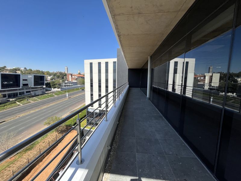 A modern, spacious balcony featuring tiled flooring, a stainless steel balustrade, and expansive glass windows overlooking the surrounding urban landscape.