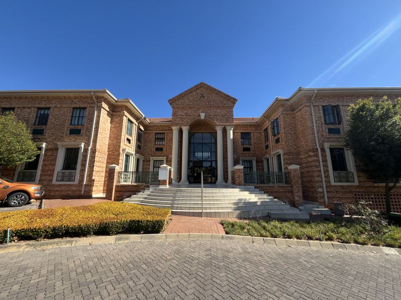A professional front elevation of a brick office building featuring classical architectural elements, a grand entrance with columns, and a paved driveway.