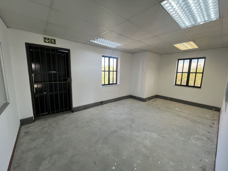 An empty office space featuring a suspended ceiling, recessed lighting, security gate, and unfinished concrete flooring, ready for final floor finishes.