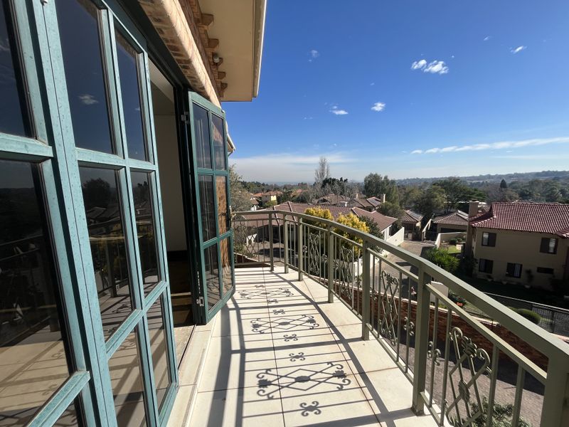 A spacious balcony featuring a decorative wrought iron balustrade, tiled flooring, and expansive views of the surrounding residential neighborhood.
