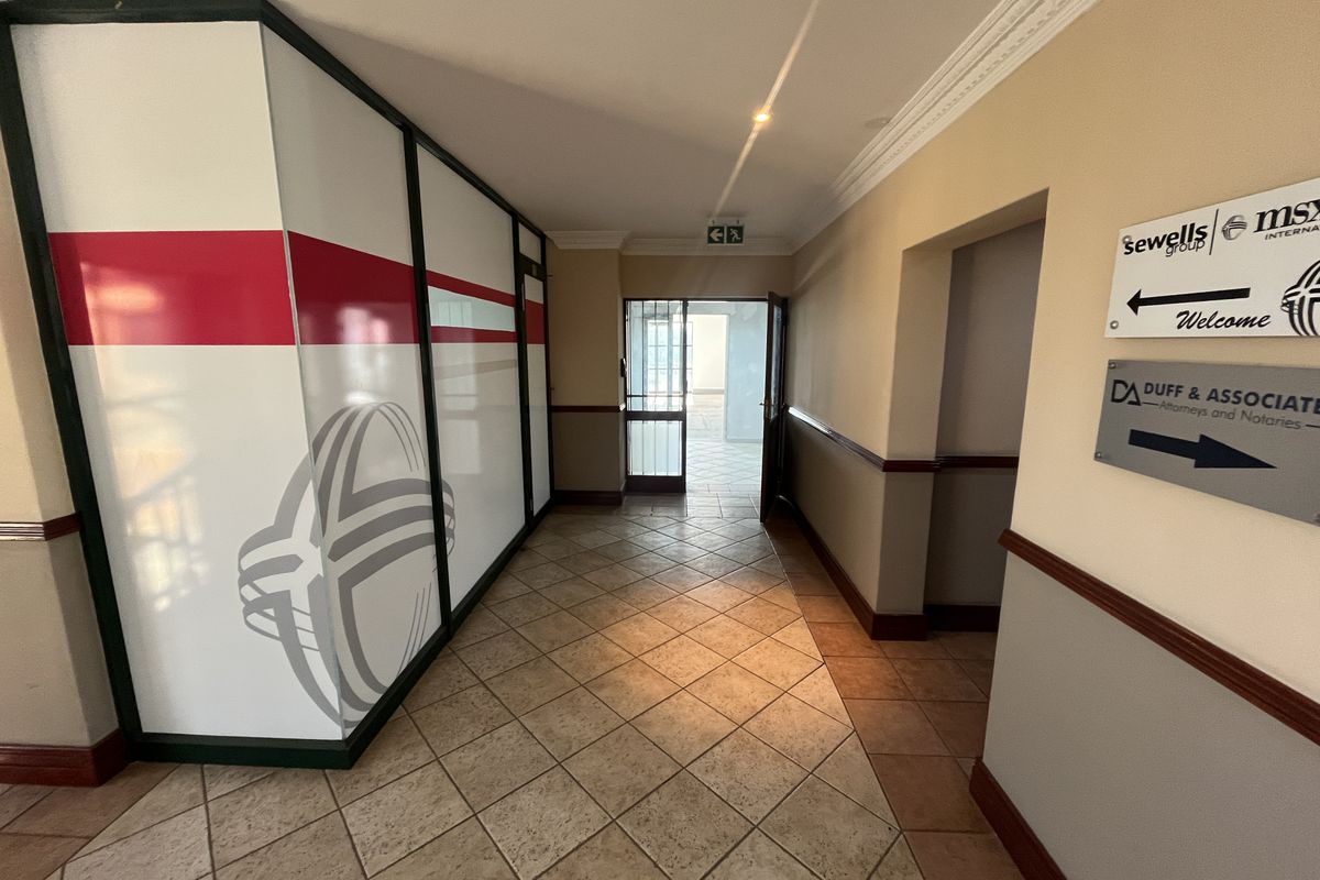 A clean office building entrance lobby featuring tiled flooring, decorative crown molding, and a glass partition wall with corporate signage.