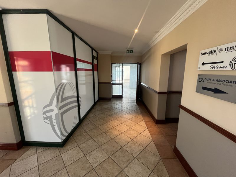 A clean office building entrance lobby featuring tiled flooring, decorative crown molding, and a glass partition wall with corporate signage.