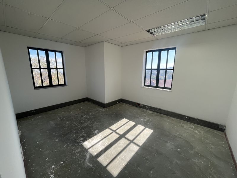 An empty office space featuring a suspended ceiling, recessed lighting, and black-framed windows, currently awaiting floor finishing.