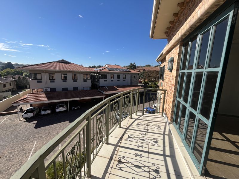 A spacious balcony featuring tiled flooring, a decorative wrought iron railing, and large glass folding doors overlooking the office complex parking area.