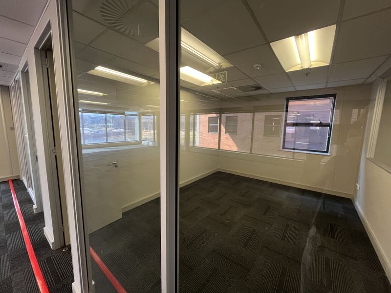 A vacant office space featuring glass partitions, carpeted flooring, and a suspended ceiling with integrated lighting.
