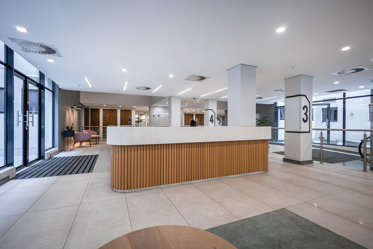 Modern office building lobby featuring a sleek reception desk, tiled flooring, and floor-to-ceiling glass windows providing ample natural light.
