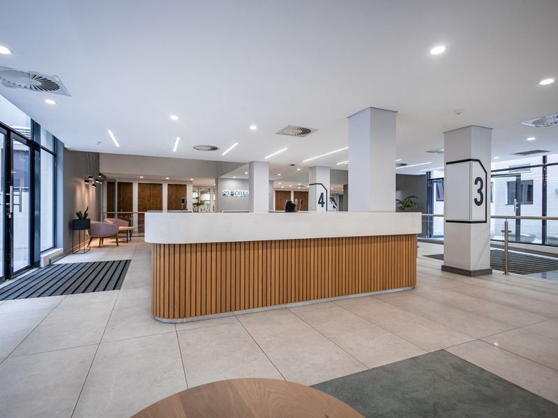 Modern office building lobby featuring a sleek reception desk, tiled flooring, and floor-to-ceiling glass windows providing ample natural light.