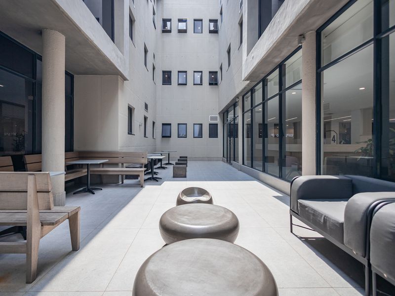 A modern, well-maintained outdoor courtyard area featuring large format tiling, concrete structural columns, and extensive glass facades providing natural light to the office building.