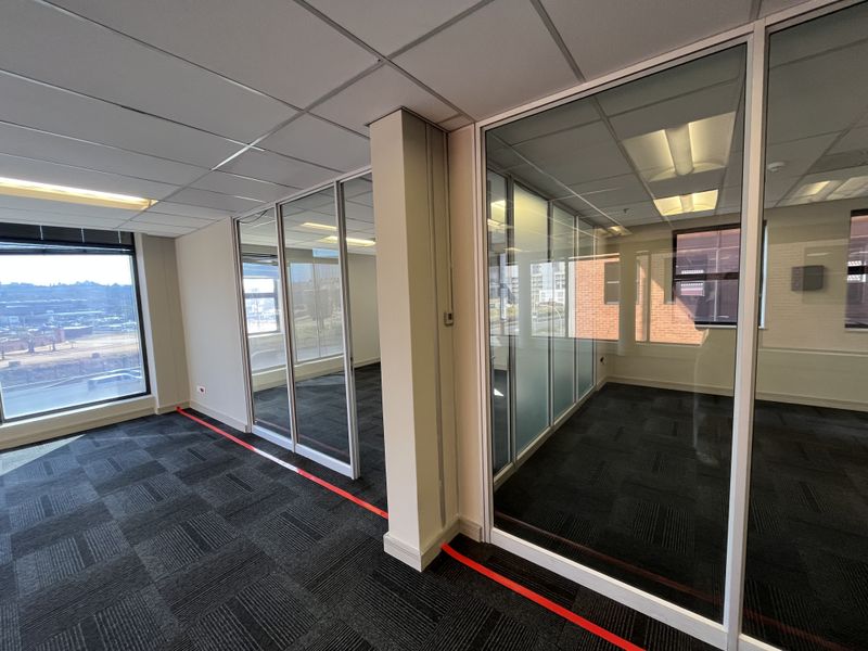 Modern office space featuring glass partition walls, carpet tiles, and a suspended ceiling with recessed lighting, offering a clean and professional work environment.