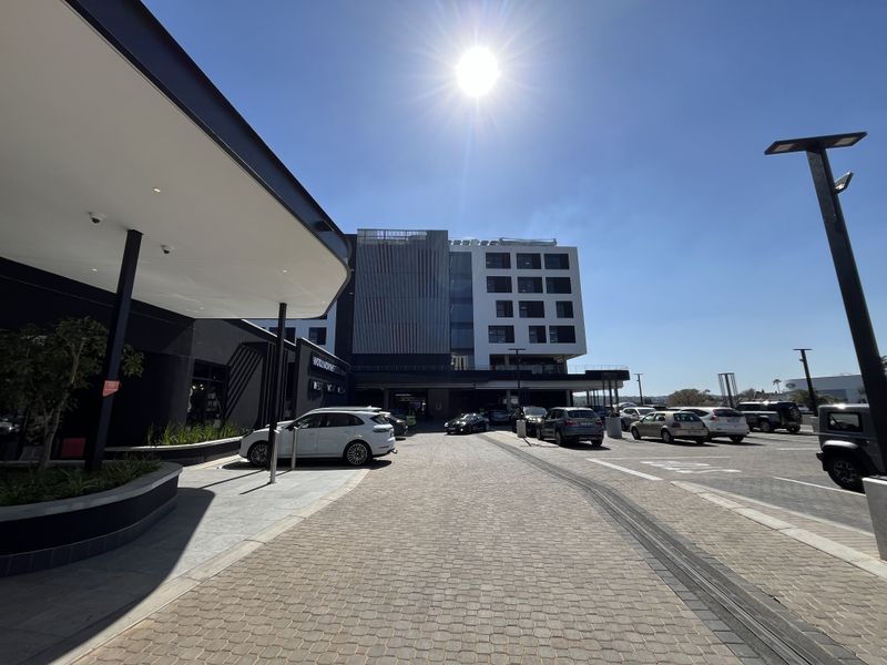 A modern office building exterior featuring a paved driveway, covered entrance canopy, and contemporary architectural facade with ample parking space.