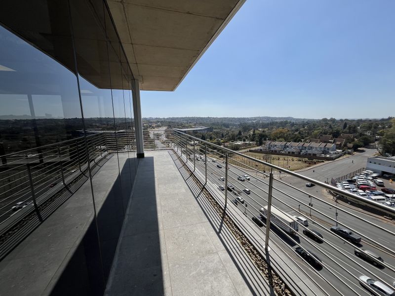 A modern, spacious balcony featuring sleek stainless steel railings, tiled flooring, and expansive glass facade offering panoramic views of the surrounding area.