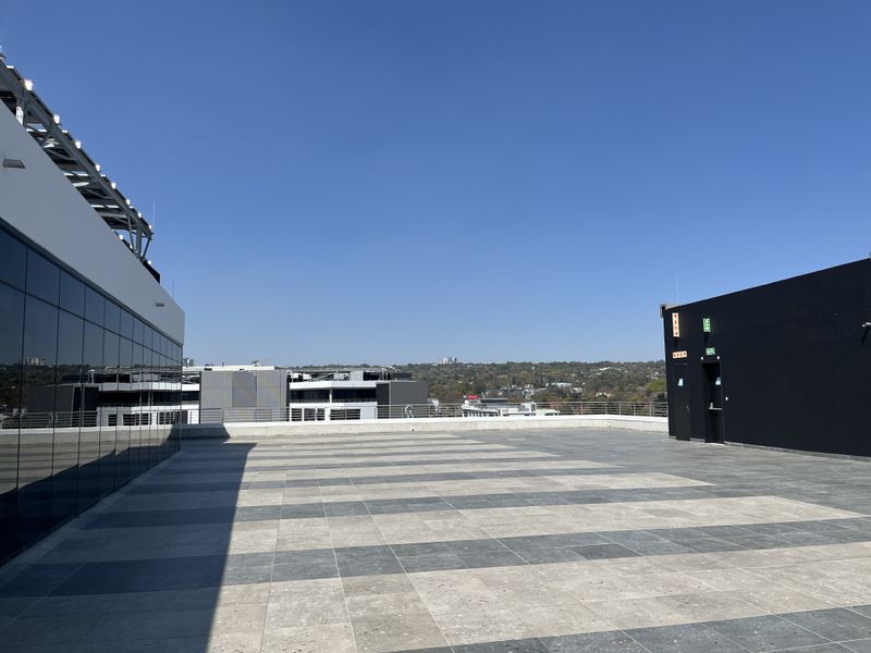 Spacious rooftop terrace featuring modern tiled flooring, glass facade, and panoramic views, suitable for outdoor office breakout space or events.