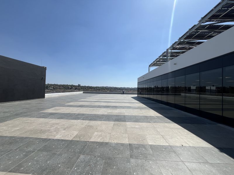 Spacious rooftop terrace featuring modern tiled flooring, glass facade, and integrated solar panel infrastructure with panoramic views.