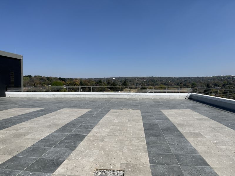 A spacious, open-air rooftop balcony featuring modern two-tone tiled flooring and a sleek stainless steel balustrade with expansive panoramic views.