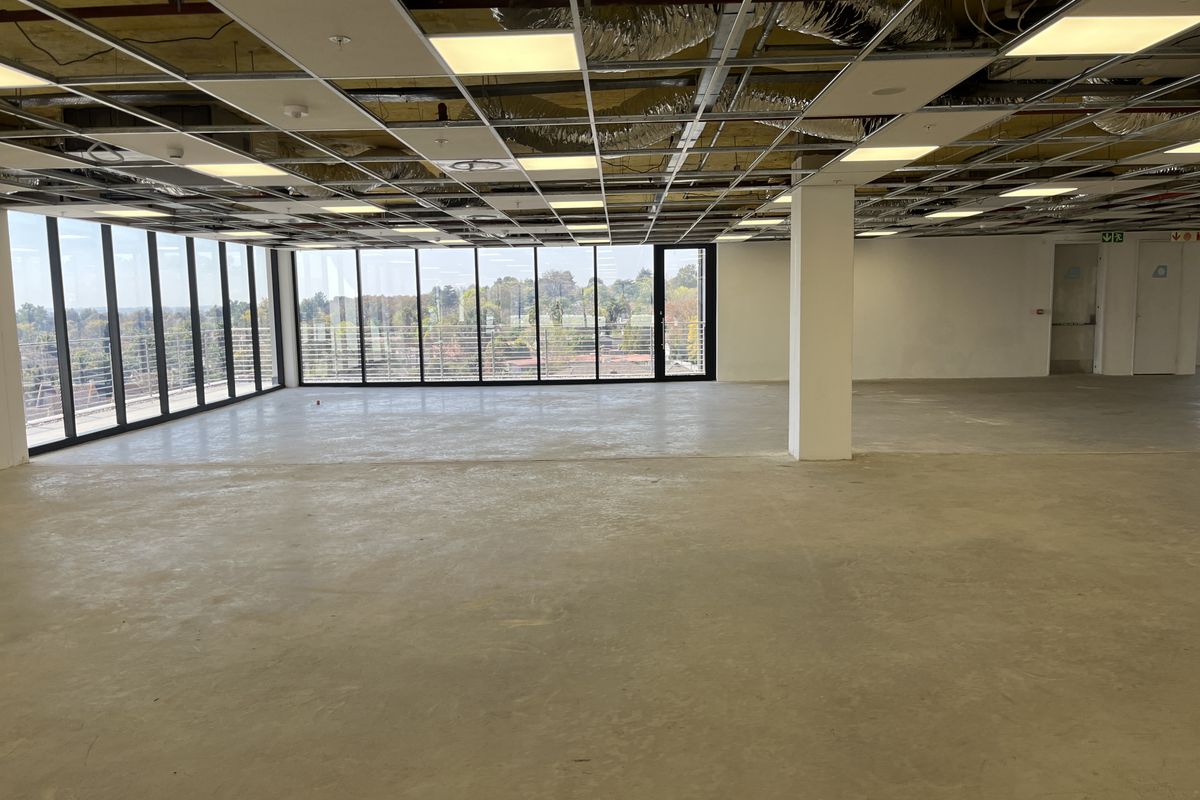 Spacious open-plan office area featuring floor-to-ceiling windows, concrete flooring, and an unfinished suspended ceiling grid, offering a blank canvas for custom fit-out.