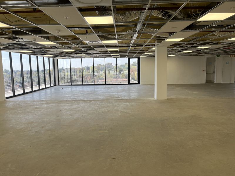 Spacious open-plan office area featuring floor-to-ceiling windows, concrete flooring, and an unfinished suspended ceiling grid, offering a blank canvas for custom fit-out.