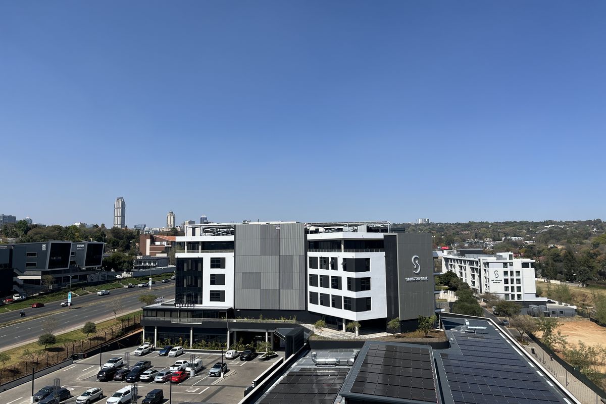 Aerial view of the office complex featuring modern building architecture, extensive rooftop solar panel installations, and an adjacent paved parking area.