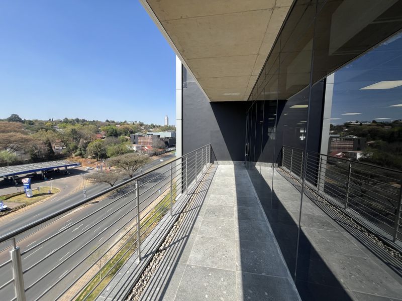 A modern office balcony featuring stone tile flooring, a stainless steel balustrade, and expansive glass facade overlooking the surrounding urban landscape.