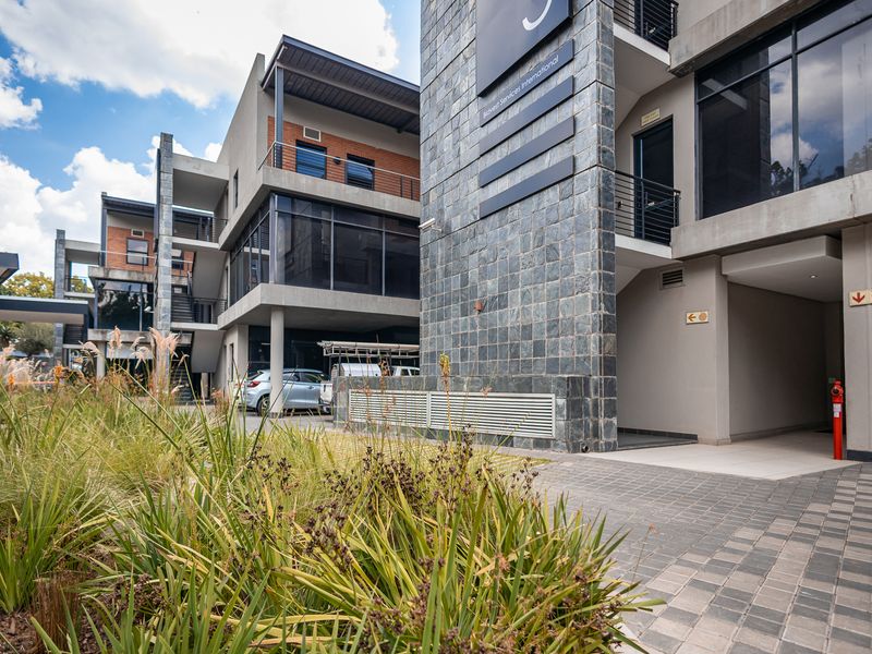 Modern multi-story office building exterior featuring stone cladding, large glass windows, and paved access areas with professional landscaping.