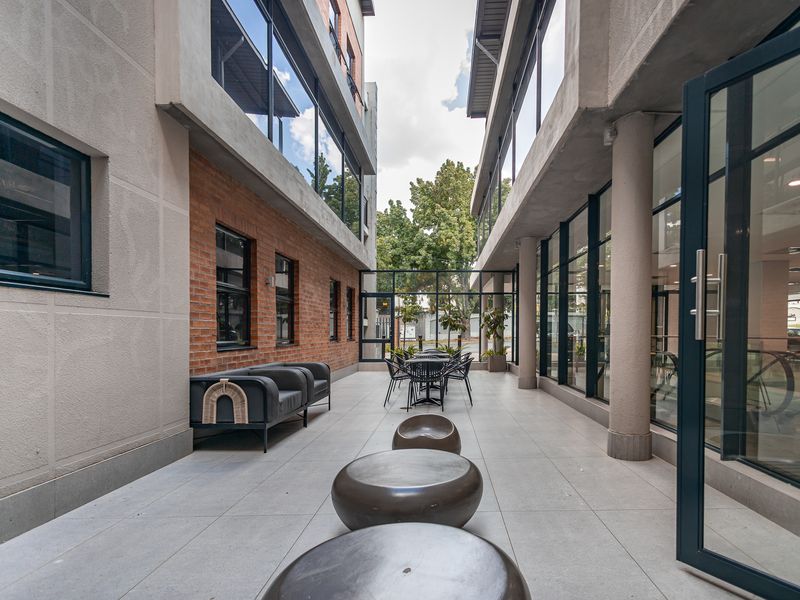 A modern, covered outdoor courtyard area featuring tiled flooring, exposed brick accents, and large glass windows connecting the office building wings.