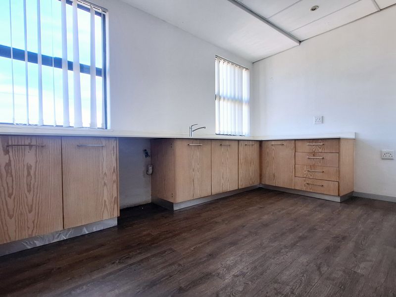 A functional office kitchenette featuring light wood-finish cabinetry, laminate countertops, and durable flooring, providing a clean and practical workspace utility area.