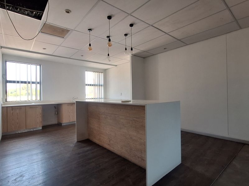 An empty office kitchen area featuring a central island, built-in cabinetry, laminate flooring, and a suspended ceiling with exposed sections.