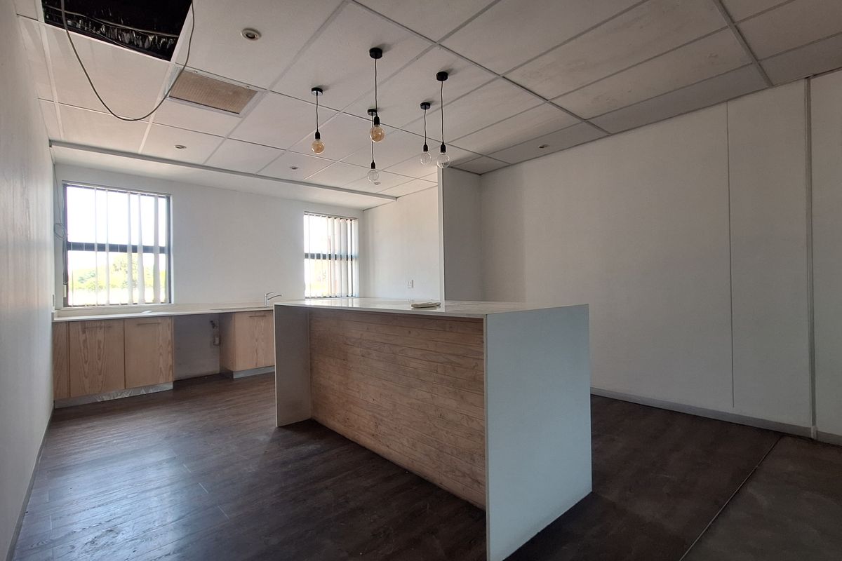 An empty office kitchen area featuring a central island, built-in cabinetry, laminate flooring, and a suspended ceiling with exposed sections.