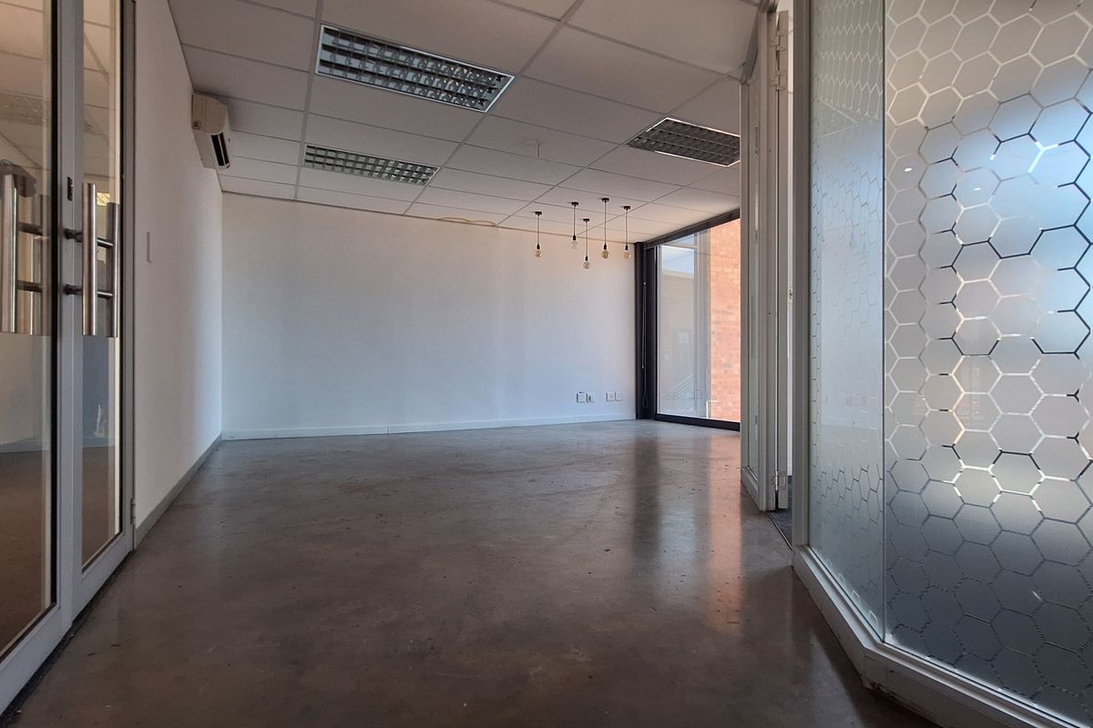 A bright, empty office space featuring polished concrete floors, a suspended ceiling with recessed lighting, and modern glass partitions with decorative frosting.