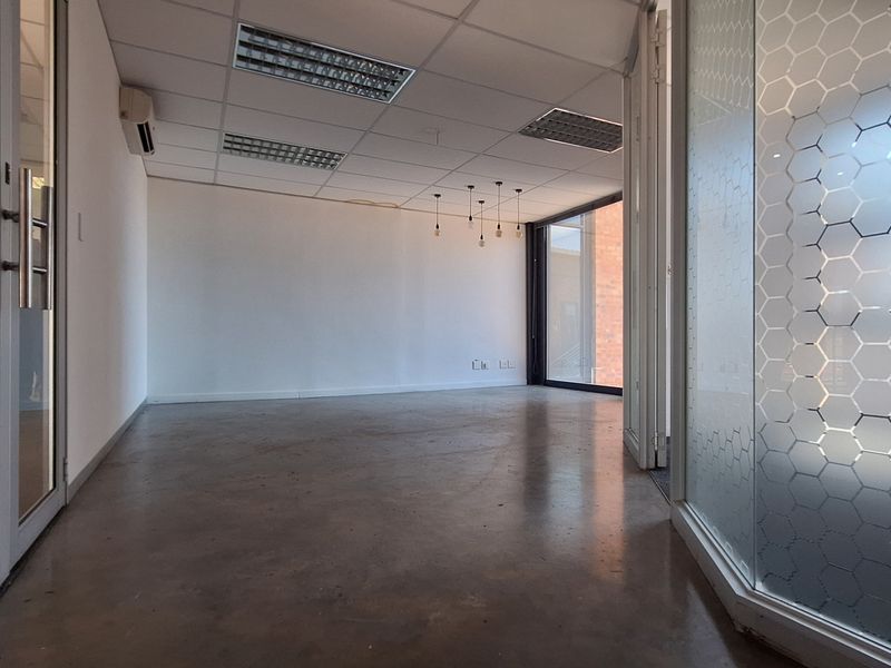 A bright, empty office space featuring polished concrete floors, a suspended ceiling with recessed lighting, and modern glass partitions with decorative frosting.