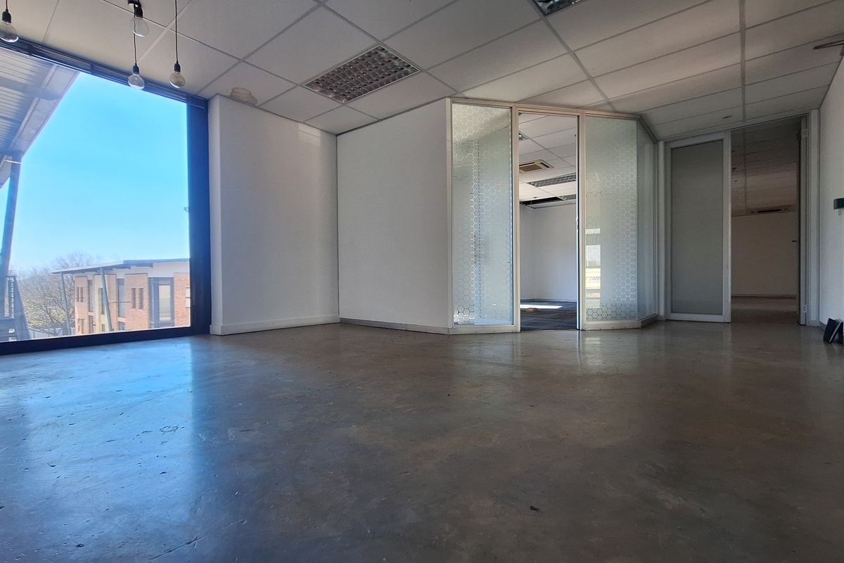 An open-plan office space featuring polished concrete floors, suspended ceilings, and glass partitions, offering a bright, modern workspace with large windows.