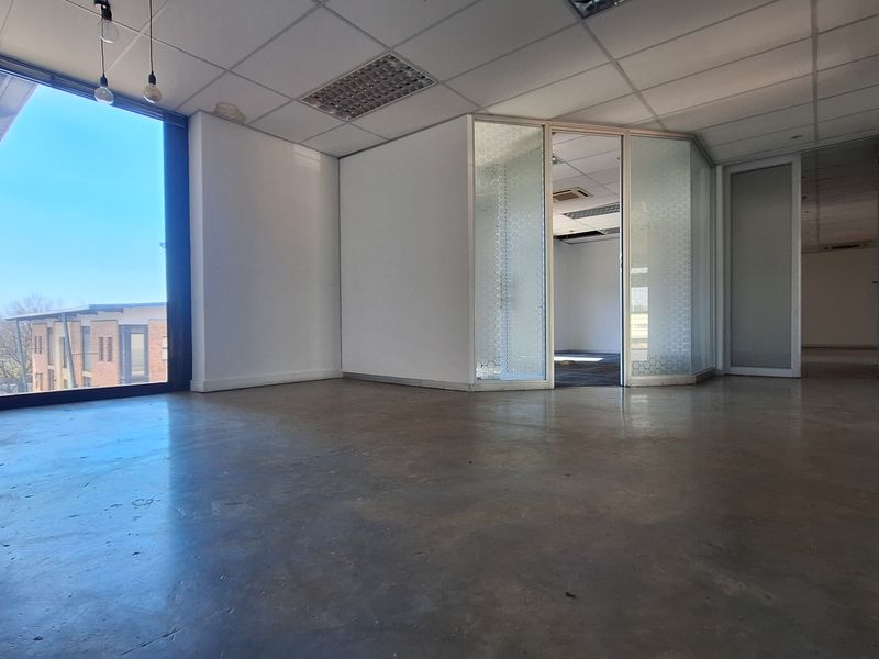 An open-plan office space featuring polished concrete floors, suspended ceilings, and glass partitions, offering a bright, modern workspace with large windows.