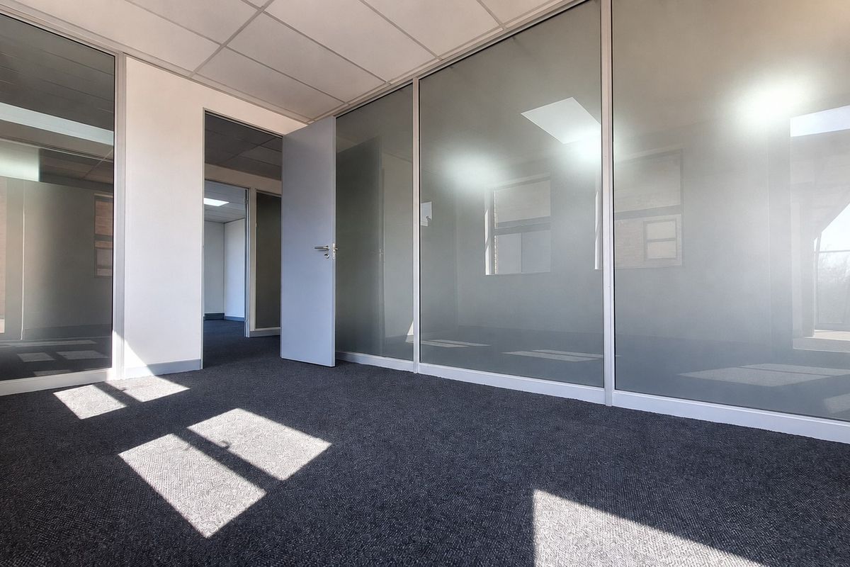 A modern, vacant office space featuring glass partition walls, suspended ceilings, and clean carpet flooring, offering a professional and bright work environment.
