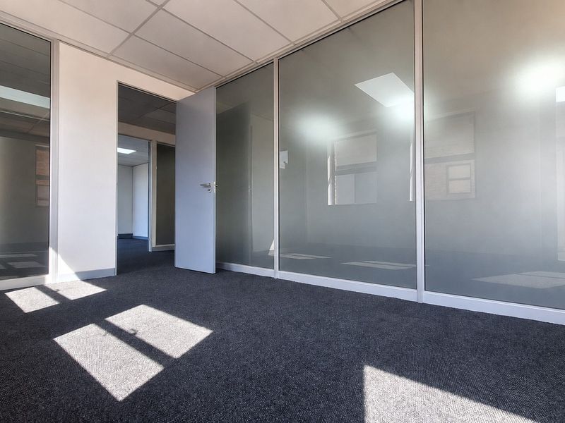 A modern, vacant office space featuring glass partition walls, suspended ceilings, and clean carpet flooring, offering a professional and bright work environment.