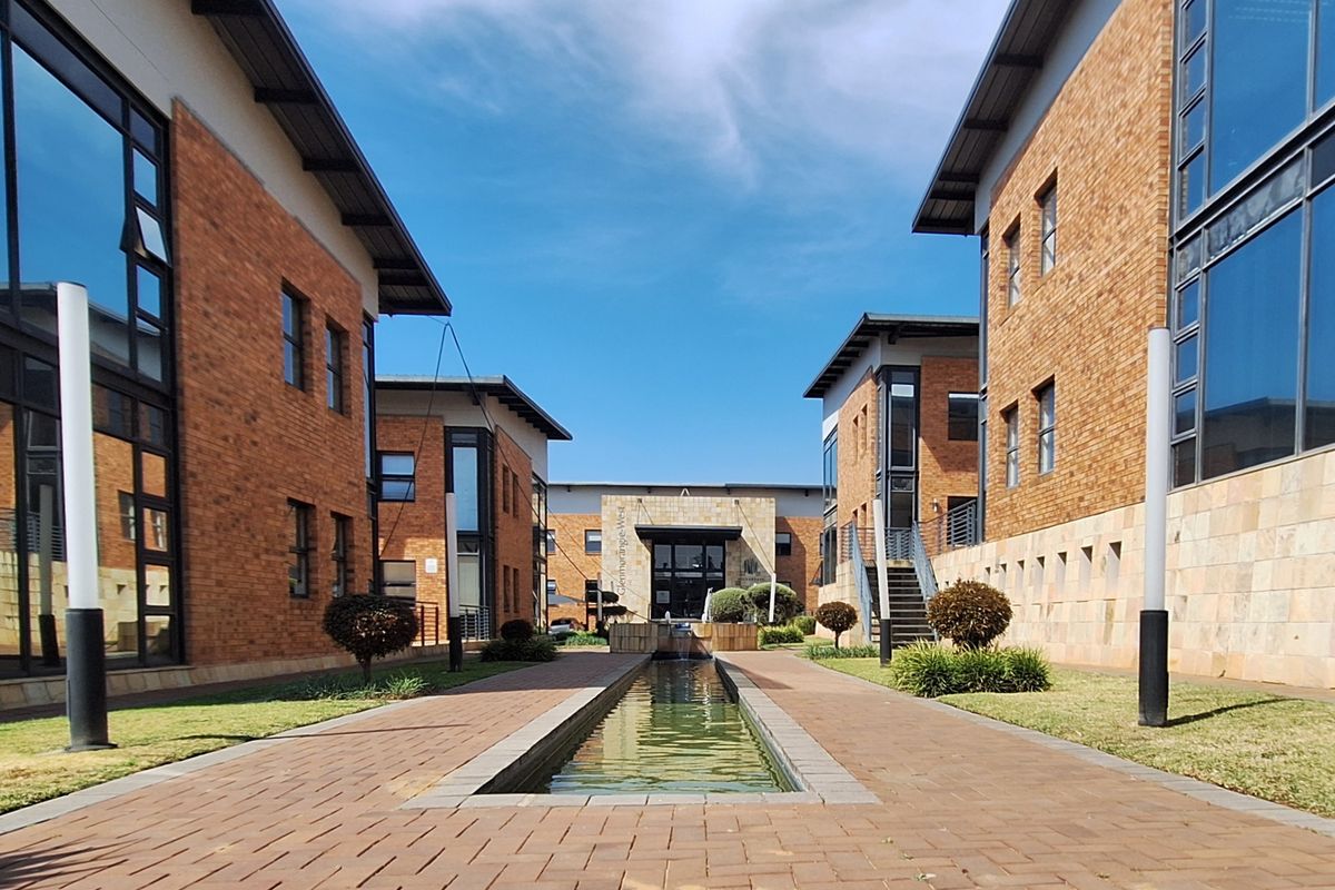 A well-maintained office complex courtyard featuring brick buildings, large glass windows, a central water feature, and paved walkways.