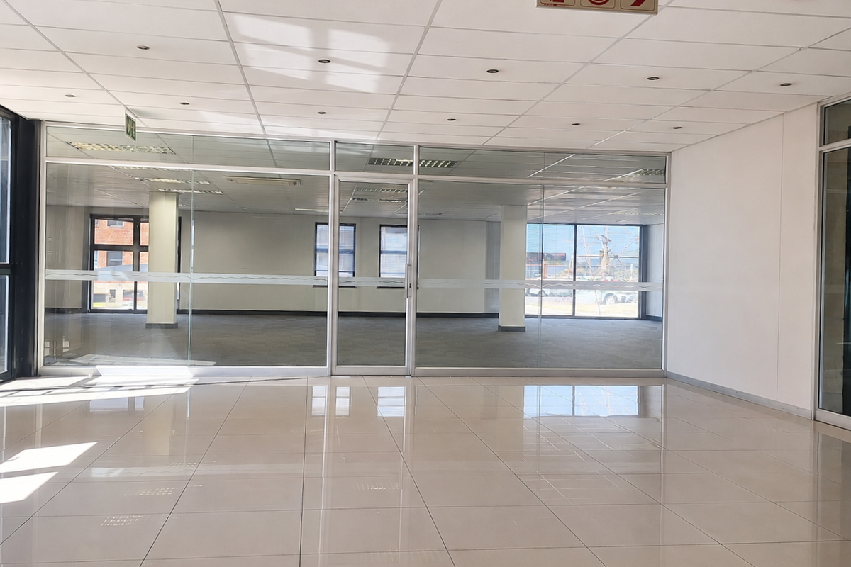 A bright, open-plan office space featuring modern glass partitioning, polished tiled flooring, and a suspended ceiling with integrated recessed lighting.