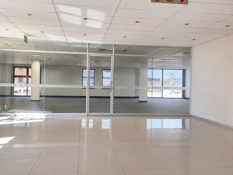A bright, open-plan office space featuring modern glass partitioning, polished tiled flooring, and a suspended ceiling with integrated recessed lighting.