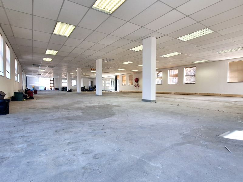 A large, open-plan office space featuring a suspended ceiling, recessed lighting, and structural columns, currently awaiting flooring installation and final finishes.
